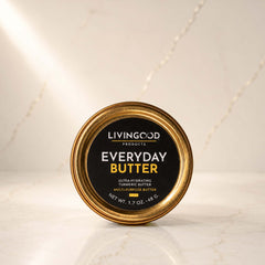 A round tin of Livingood Products Everyday Butter, featuring a black label with gold and white text, set on a light marble surface with a matching marble background.