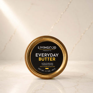A round tin of Livingood Products Everyday Butter, featuring a black label with gold and white text, set on a light marble surface with a matching marble background.