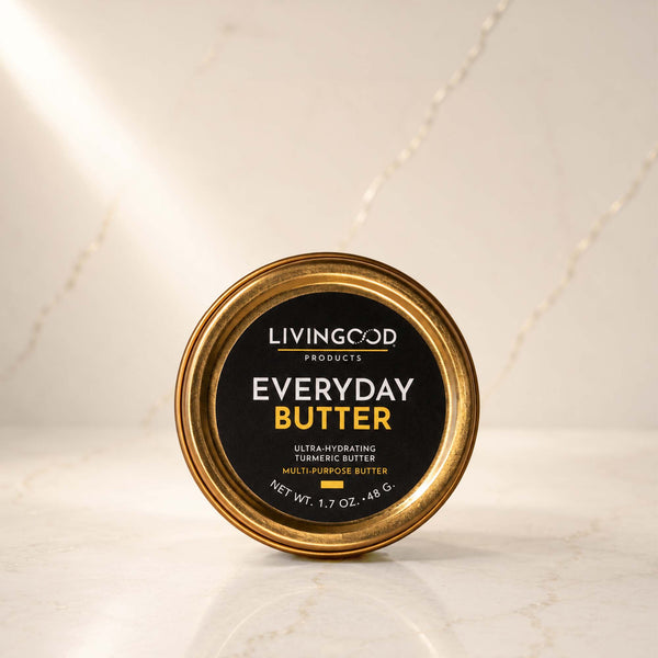 A round tin of Livingood Products Everyday Butter, featuring a black label with gold and white text, set on a light marble surface with a matching marble background.