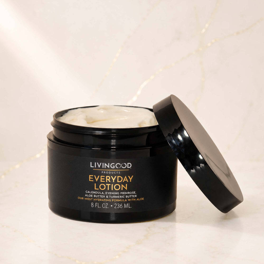Livingood Skincare Everyday Lotion in an open black jar with its lid leaning against it, showing the white lotion inside, set on a light marble surface.