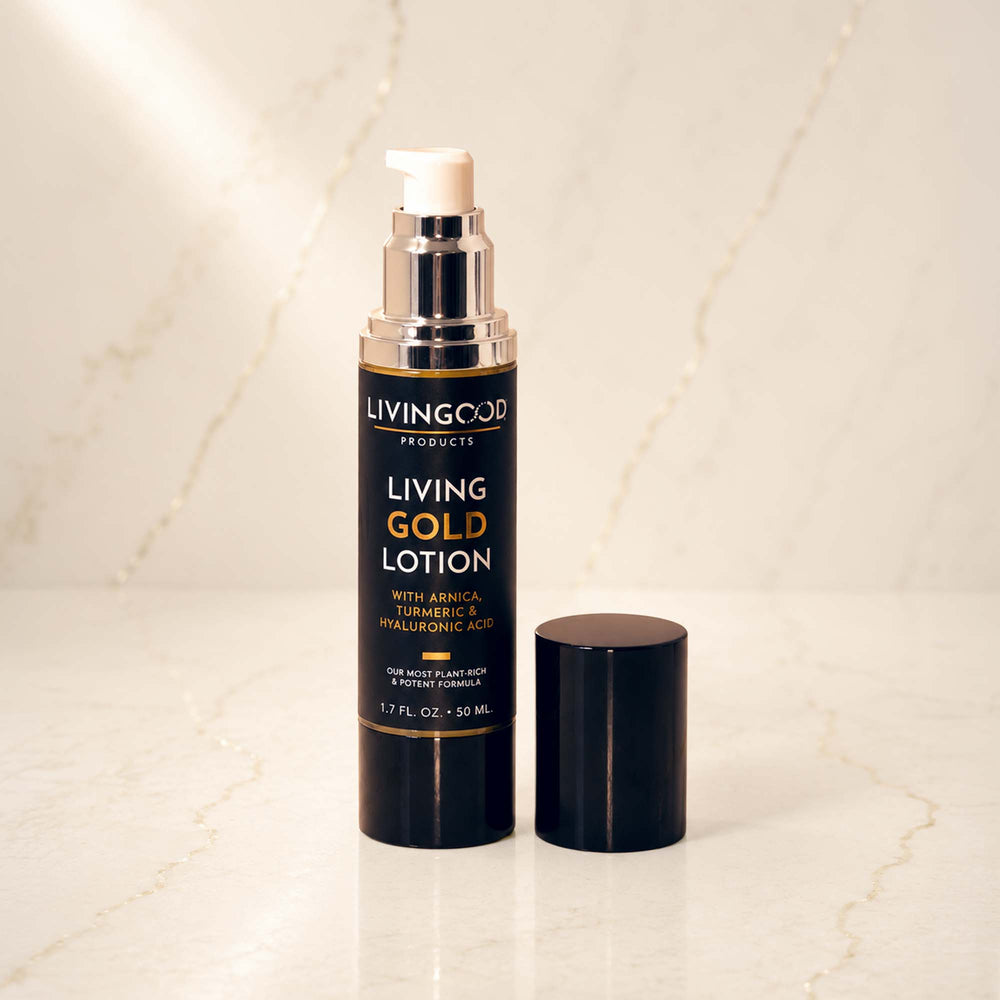 Living Gold Lotion pump bottle with its cap off, standing on a light marble surface against a matching marble background. The bottle is black with gold lettering and a white pump dispenser.