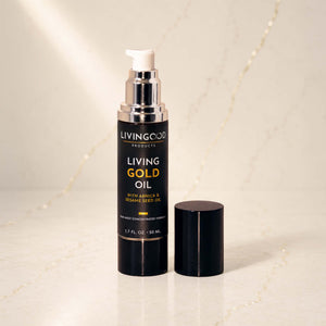 Living Gold Oil pump bottle with its cap off, displayed on a light marble surface with a soft-focus background.