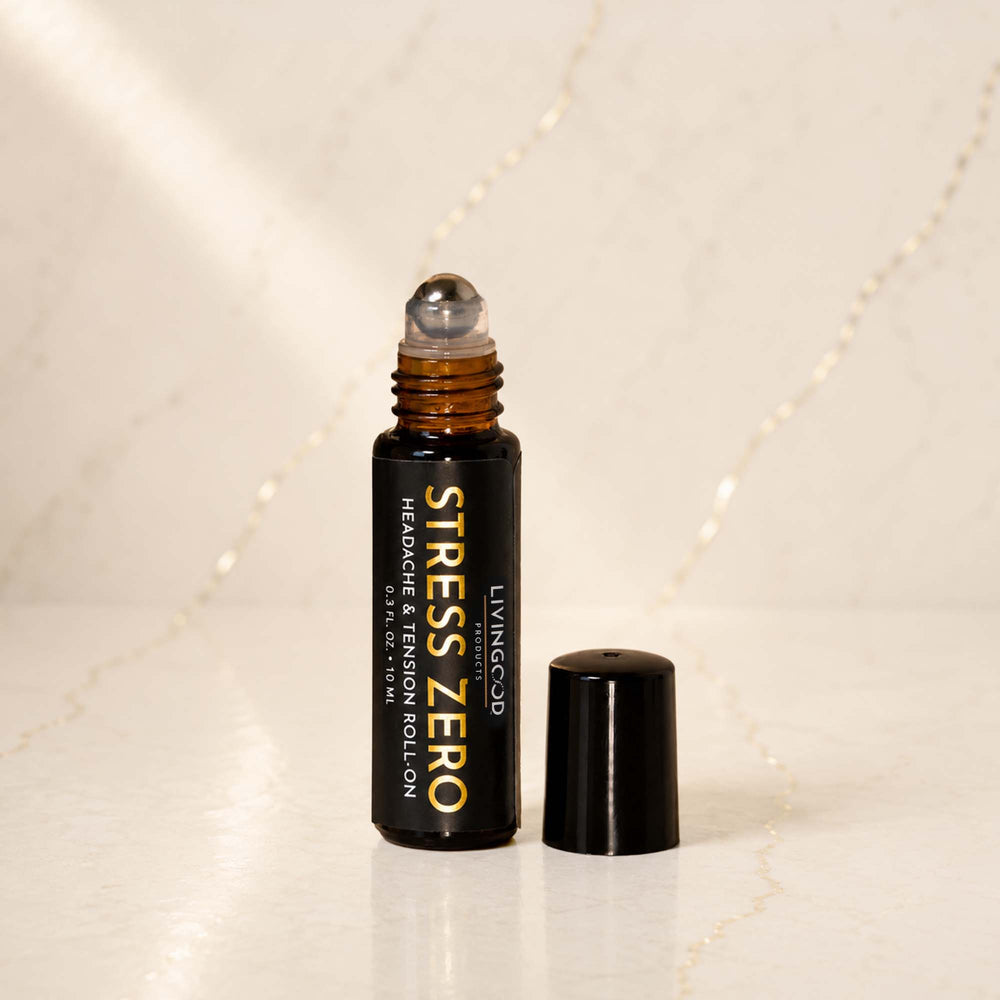 A bottle of LIVINGOOD Stress Zero Headache & Tension Roll-On with its cap off, standing on a light marble surface with a marble background.
