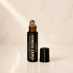 A bottle of LIVINGOOD Stress Zero Headache & Tension Roll-On with its cap off, standing on a light marble surface with a marble background.