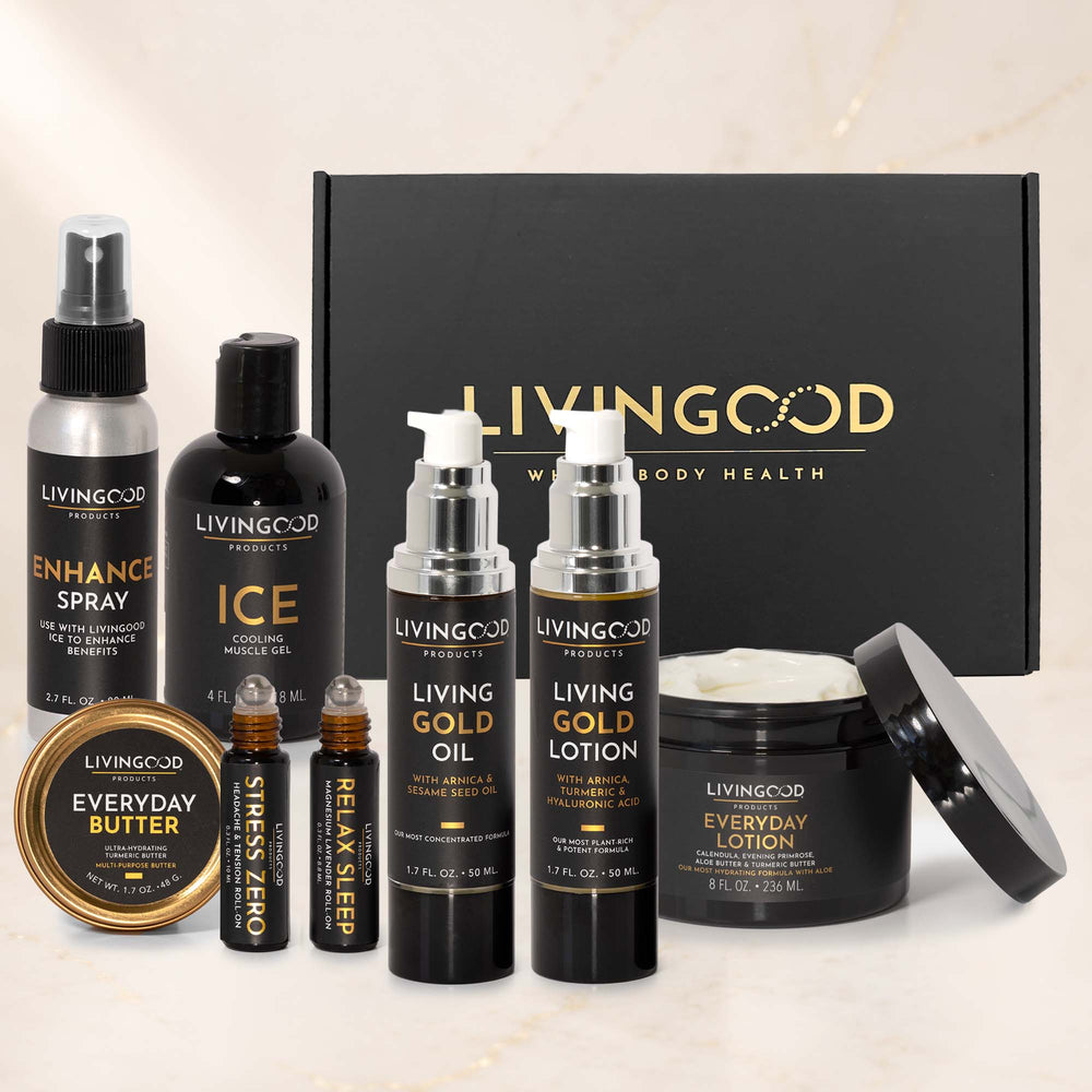 A Livinggood body care gift set arranged in front of a black gift box on a light marble background. The set includes an Everyday Butter jar, an Enhance Spray bottle, an Ice bottle, a Living Gold Oil bottle, a Living Gold Lotion bottle, a Stress & Relax roller bottle, and a jar of Everyday Lotion with its lid leaning beside it.